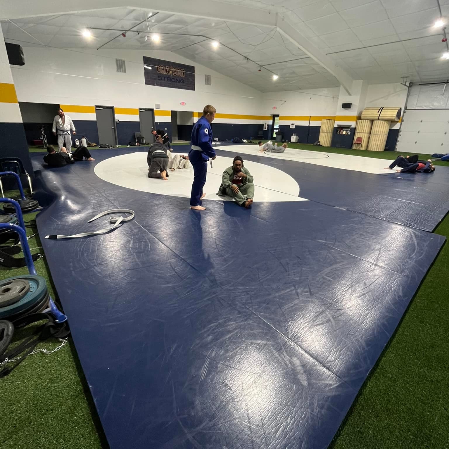 Adults in gi warming up and drilling on the mats at the Grayson High School Annex training facility